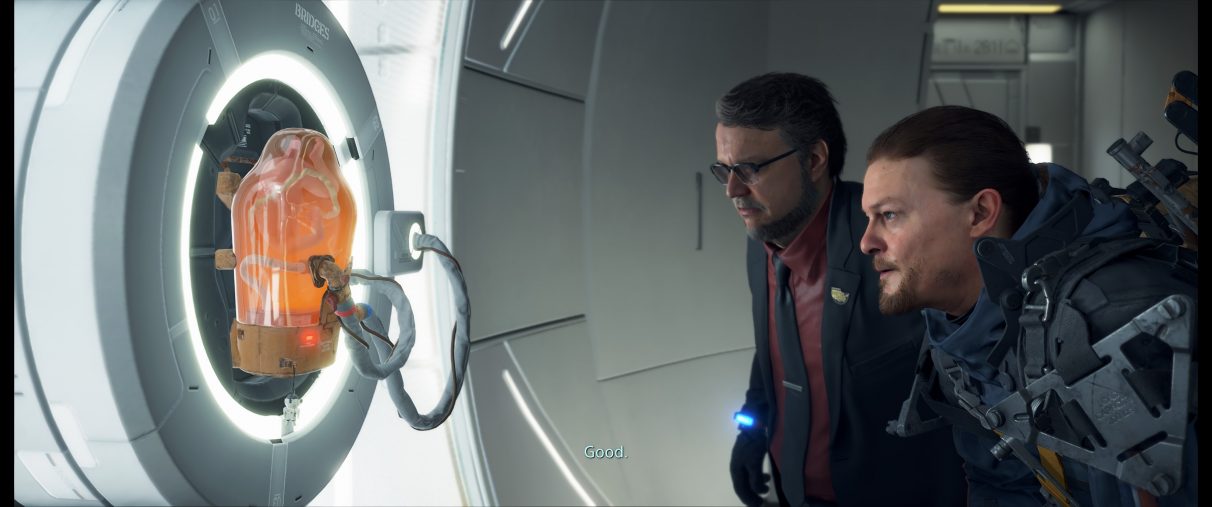 A screenshot of Death Stranding's Sam Bridges and Deadman inspecting a sleeping BB in an ultrawide aspect ratio.