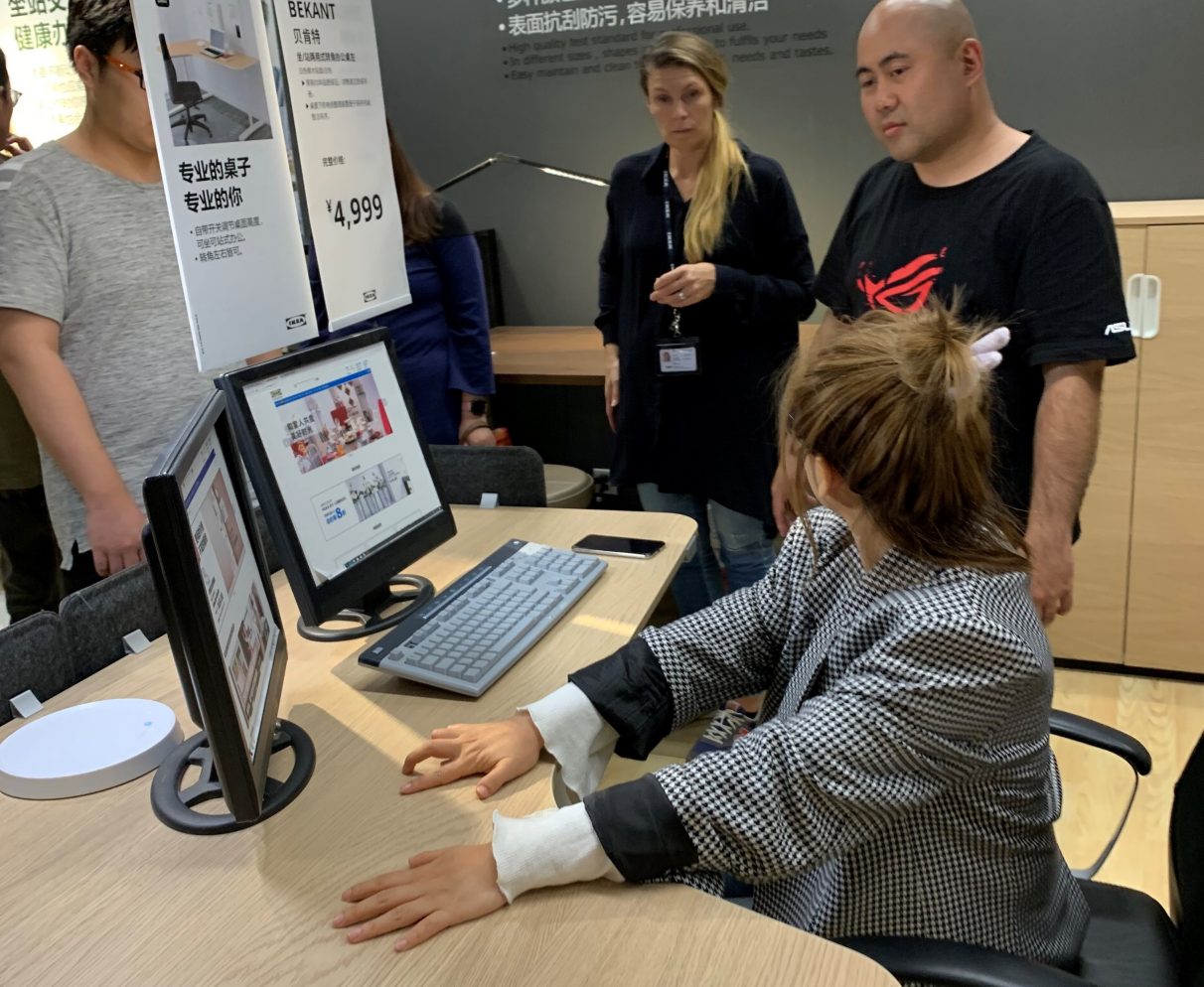 An photo from one of Asus and Ikea's design workshops, showing an Asus representative standing beside a woman seated at an existing Ikea desk.