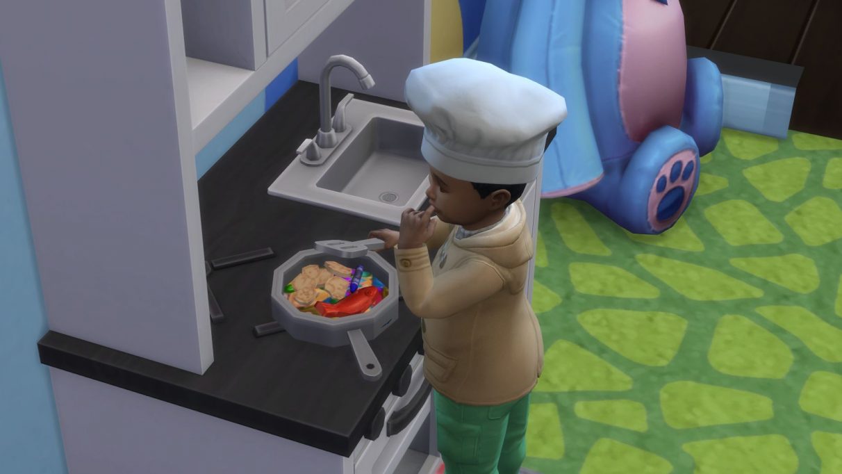 A screenshot of a toddler using the custom content play kitchen in The Sims 4. He is stirring a pan full of crayons and other small toys, and has raised a finger to his lips as if to taste test it. He is wearing a small chef's hat.